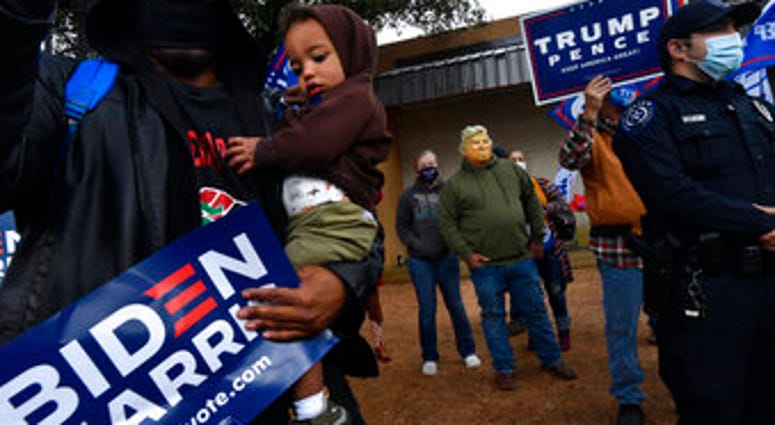 Demetrius Earthly balances his one-year-old son Brodrick and a Biden-Harris campaign sign, Wednesday, Oct. 28, 2020. Behind him, Toby Lindley wears a Donald Trump mask. (Ronald W. Erdrich/The Abilene Reporter-News via AP) Demetrius Earthly balances his one-year-old son Brodrick and a Biden-Harris campaign sign, Wednesday, Oct. 28, 2020. Behind him, Toby Lindley wears a Donald Trump mask. (Ronald W. Erdrich/The Abilene Reporter-News via AP)
