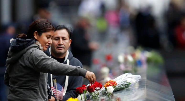 A woman drips water on a bouquet of flowers at the North Pool during a ceremony marking the 17th anniversary of the terrorist attacks on the United States on Tuesday, Sept. 11, 2018, in New York. (AP Photo/Mark Lennihan)