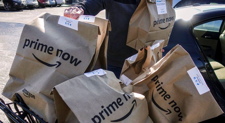FILE - In this Feb. 8, 2018, file photo, Amazon Prime Now bags full of groceries are loaded for delivery by a part-time worker outside a Whole Foods store in Cincinnati. Amazon’s Prime Day deals are coming to the aisles of Whole Foods, as the online retai