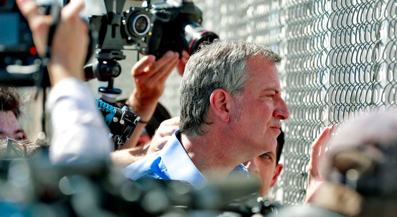 In this Thursday, June 21, 2018, file photo, New York City Mayor Bill de Blasio looks through a closed gate at the Port of Entry facility, in Fabens, Texas. (AP Photo/Matt York, File)