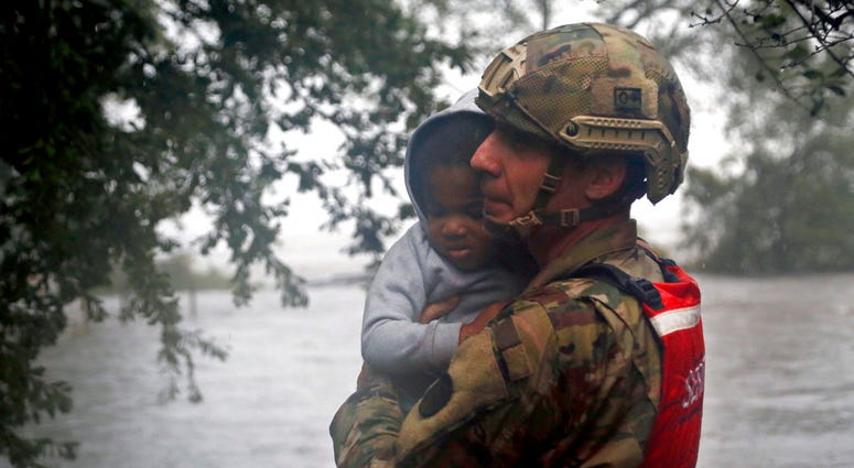 Rescue team member Sgt. Nick Muhar, from the North Carolina National Guard 1/120th battalion, evacuates a young child as the rising floodwaters from Hurricane Florence threatens his home in New Bern, N.C., on Friday, Sept. 14, 2018