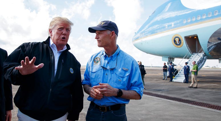 Gov. Rick Scott, R-Fla., right, looks on as President Donald Trump talks with reporters after arriving at Eglin Air Force Base to visit areas affected by Hurricane Michael, Monday, Oct. 15, 2018, in Eglin Air Force Base, Fla.