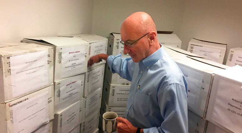 In this Aug. 7, 2018, photo, Mark Robbins, the sole member of the Merit Systems Protection Board, walks through the supply closet, pointing to boxes full of cases, in his office in Washington.