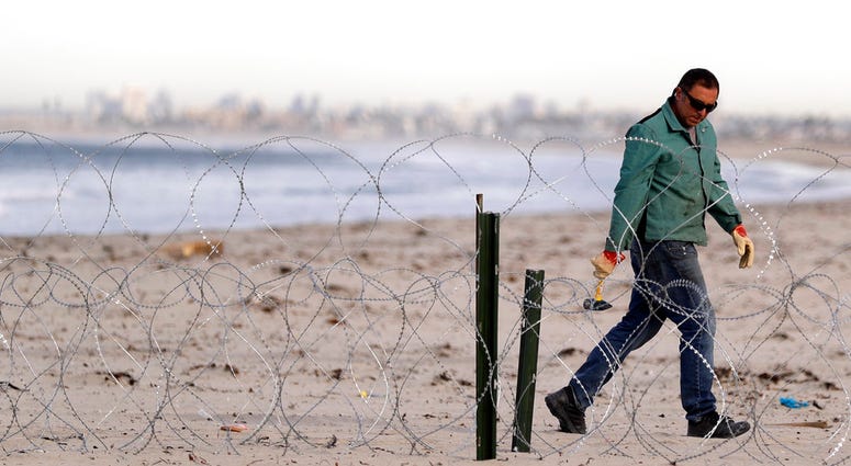 A worker installs concertina wire along the beach closest to the border, as the city of San Diego sits in the distance, as seen from Tijuana, Mexico, Wednesday, Nov. 14, 2018. (AP Photo/Gregory Bull)