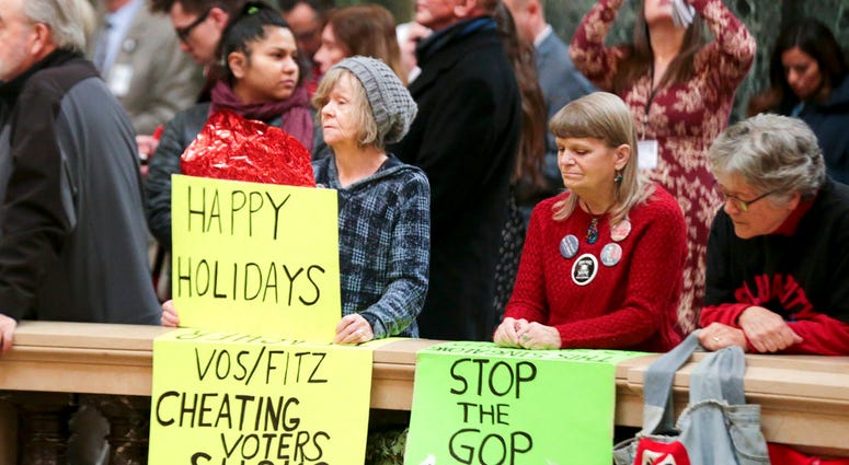 Protesters Peppi Elder, left, and Christine Taylor holds up signs during the state Christmas Tree lighting ceremony in state Capitol Rotunda Tuesday Dec. 4, 2018, in Madison, Wis.
