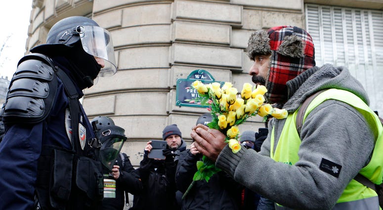 A demonstrator wearing his yellow vest holds a bouquet of roses in front of a riot police officer during a protest Saturday, Dec. 15, 2018 in Paris
