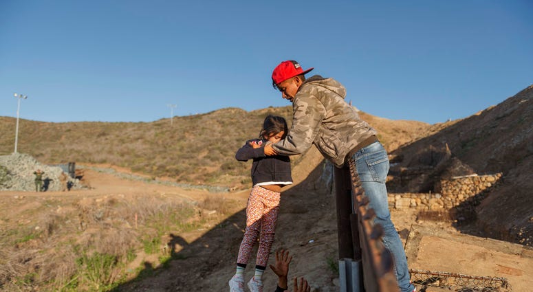 A migrant from Honduras pass a child to her father after he jumped the border fence to get into the U.S. side to San Diego, Calif., from Tijuana, Mexico, Thursday, Jan. 3, 2019.