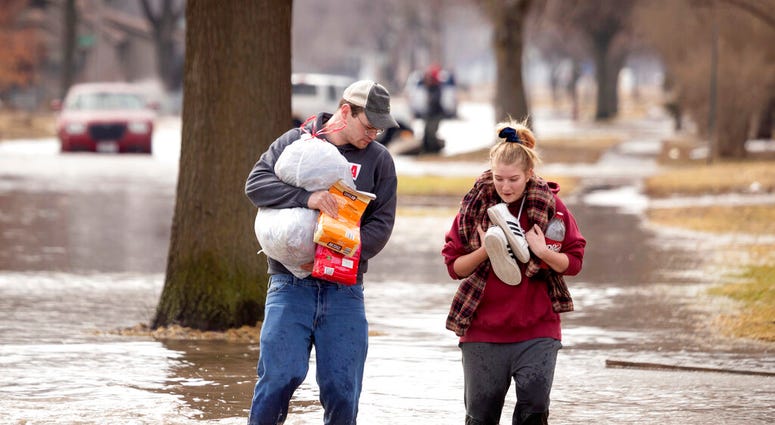 Anthony Thomson, left, and Melody Walton make their way out of a flooded neighborhood Sunday, March 17, 2019, in Fremont, Neb. (Kent Sievers/Omaha World-Herald via AP) Anthony Thomson, left, and Melody Walton make their way out of a flooded neighborhood Sunday, March 17, 2019, in Fremont, Neb. (Kent Sievers/Omaha World-Herald via AP)