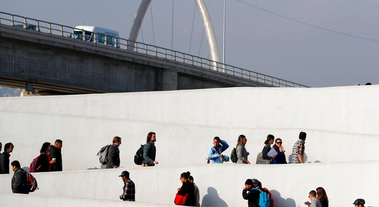 FILE - In this Tuesday, March 19, 2019, file photo, a man who only gave his first name as Ariel, of Honduras, center in blue shirt, crosses into the United States to begin his asylum case with others after being returned to Mexico in Tijuana, Mexico. A U.