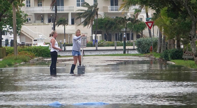 In this Oct. 5, 2017, file photo, residents move a "no wake," sign through flood waters caused by king tides in Fort Lauderdale, Fla. (Joe Cavaretta/South Florida Sun-Sentinel via AP)