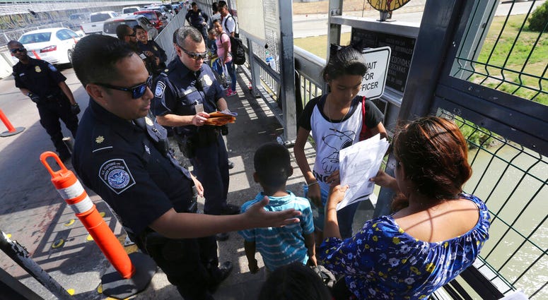 FILE - In this July 17, 2019, file photo, a United States Customs and Border Protection Officer checks the documents of migrants before being taken to apply for asylum in the United States, on International Bridge 1 in Nuevo Laredo, Mexico. On Wednesday,