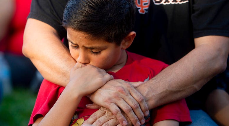 Robbie Ramirez, 10, holds onto his father, Robert Ramirez, during a vigil for victims of a Sunday evening shooting that left three people dead at the Gilroy Garlic Festival, Monday, July 29, 2019, in Gilroy, Calif. (AP Photo/Noah Berger)