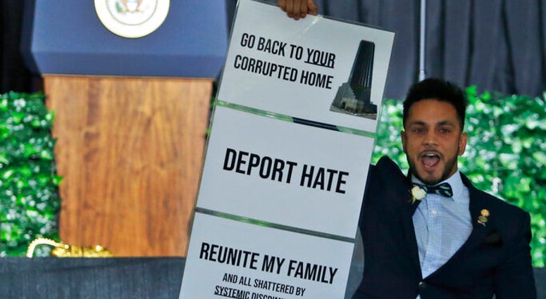 President Donald Trump waits as Virginia Delegate Ibraheem S. Samirah, D-Fairfax, holds a sign and interrupts a speech by Trump as he addresses a commemorative meeting of the Virginia General Assembly at Jamestown Settlement. (AP Photo/Steve Helber)