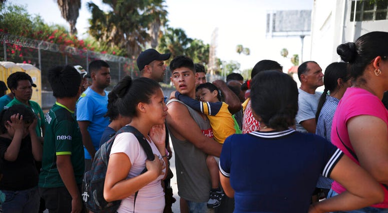In this Aug. 1, 2019, photo, migrants line up in Matamoros, Mexico, for a meal donated by volunteers from the U.S., at the foot of the Puerta Mexico bridge that crosses to Brownsville, Texas. Turning Mexican border cities into waiting rooms for asylum see