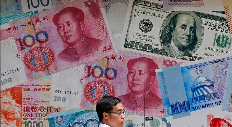 FILE - In this June 10, 2019, file photo, a man walks past a money exchange shop decorated with different banknotes at Central, a business district of Hong Kong. China's yuan fell below the politically sensitive level of seven to the U.S. dollar on Monday