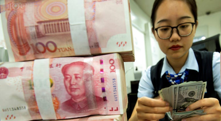 A bank employee counts U.S. dollar banknotes next to stack of 100 Chinese yuan notes at a bank outlet in Hai'an in eastern China's Jiangsu province, Tuesday, Aug. 6, 2019. China's yuan fell further Tuesday against the U.S. dollar, fueling fears about incr