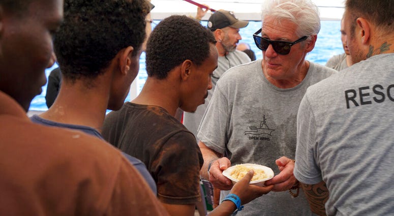 Actor Richard Gere, right, helps serving meals to migrants aboard the Open Arms Spanish humanitarian boat as it cruises in the Mediterranean Sea, Friday, Aug. 9, 2019. Open Arms has been carrying 121 migrants for a week in the central Mediterranean awaiti