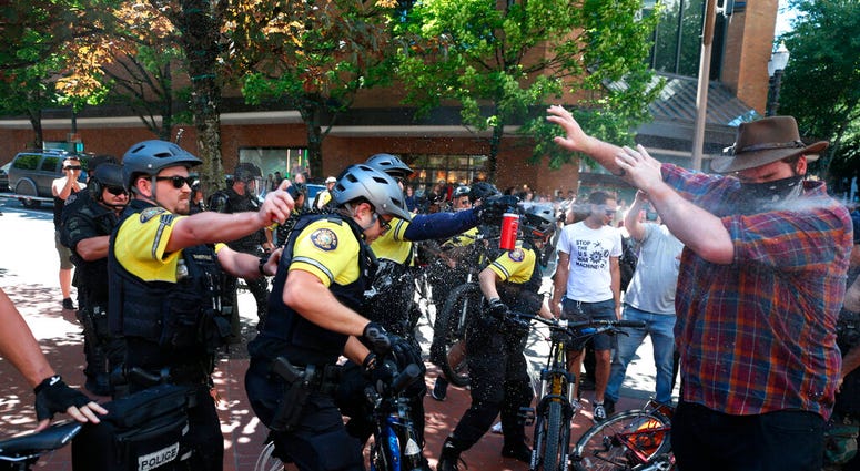 In this June 29, 2019, file photo, after a confrontation between authorities and protesters, police use pepper spray as multiple groups, including Rose City Antifa, the Proud Boys and others protest in Portland. (Dave Killen/The Oregonian via AP, File)