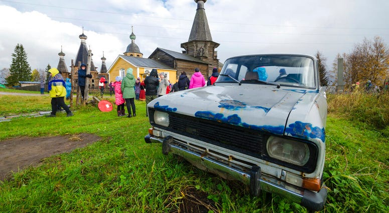 In this photo taken on Oct. 7, 2018, people walk the street with the 18th century Trinity Church in the background in the village of Nyonoksa, northwestern Russia. (AP Photo/Sergei Yakovlev)