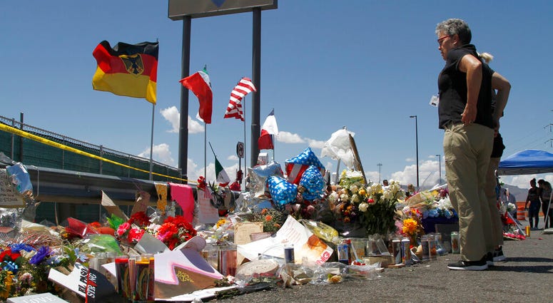 In this Aug. 12, 2019 photo, mourners visit the makeshift memorial near the Walmart in El Paso, Texas, where 22 people were killed in a mass shooting that police are investigating as a terrorist attack targeting Latinos. The flags show the nationalities o