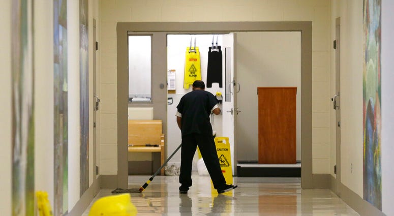 FILE - In this June 21, 2017, file photo, a detainee mops a floor in a hallway of the Northwest Detention Center in Tacoma, Wash., during a media tour of the facility.