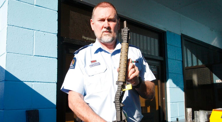 In this Aug. 31, 2019, photo. Police Senior Sgt. Braydon Lenihan poses holding a banned gun that has been bent by a hydraulic machine outside a temporary gun collection venue in Porirua, near Wellington, New Zealand.