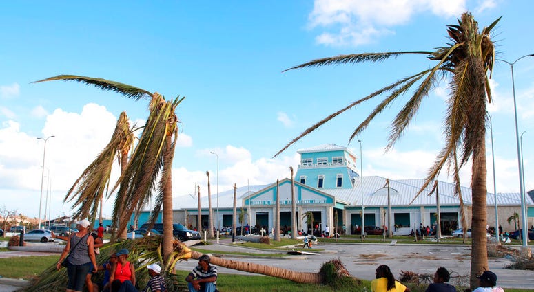 People sit under broken palm trees outside the Leonard M. Thompson International Airport after the passing of Hurricane Dorian in Marsh Harbour, Abaco Islands, Bahamas, Thursday, Sept. 5, 2019.