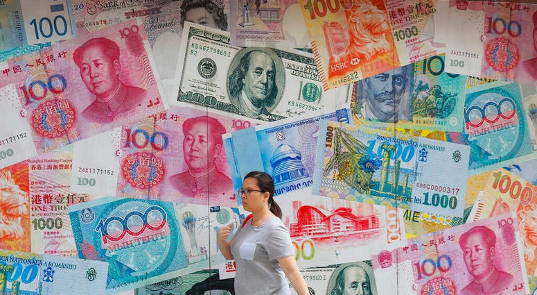 FILE - In this Aug. 6, 2019, file photo, a woman walks by a money exchange shop decorated with different countries currency banknotes at Central, a business district in Hong Kong. China's trade with the United States fell sharply in August as a tariff war