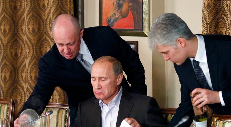FILE - In this Friday, Nov. 11, 2011, file photo, businessman Yevgeny Prigozhin, left, serves food to Russian Prime Minister Vladimir Putin, center, during dinner at Prigozhin's restaurant outside Moscow, Russia.