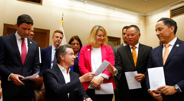 California Gov. Gavin Newsom, seated hands Assemblyman Phil Ting, D-San Francisco, second from right, a copy of his bill that Newsom signed at the Capitol in Sacramento, Calif., Friday, Oct. 11, 2019. (AP Photo/Rich Pedroncelli)