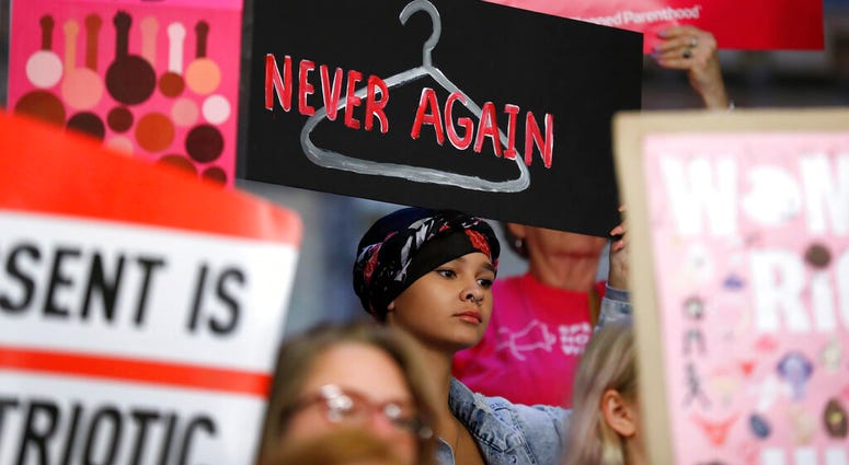 In this Tuesday, May 21, 2019 file photo, August Mulvihill, of Norwalk, Iowa, center, holds a sign depicting a wire clothes hanger during a rally at the Statehouse in Des Moines, Iowa, to protest recent abortion bans. (AP Photo/Charlie Neibergall)