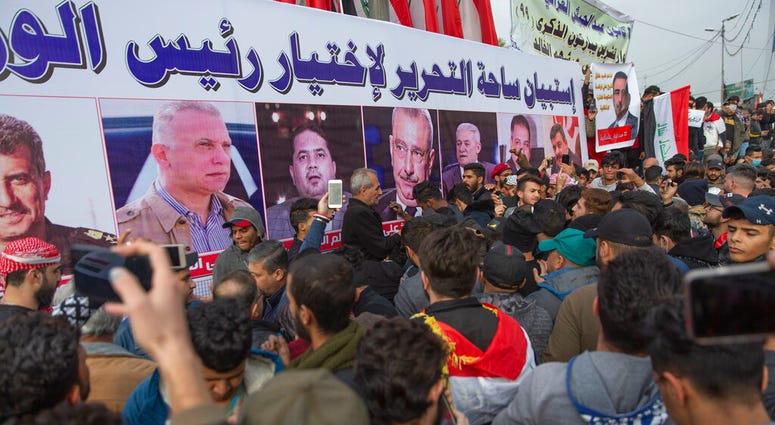 Anti government Iraqi protesters gather by a banner with pictures of Iraqi politicians and Arabic that reads "the Tahrir square questionnaire to select a prime minister," during the ongoing protests in Tahrir square, Baghdad, Iraq, Friday, Jan. 10, 2020.