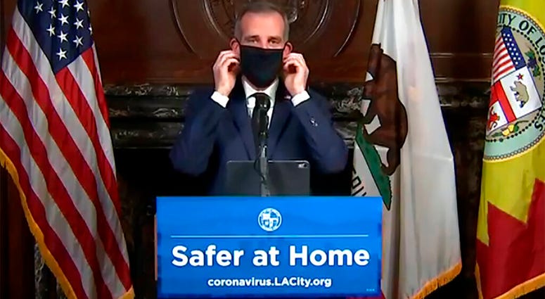 This still image taken from a live stream provided by Office of Mayor Eric Garcetti showing Los Angeles Mayor Garcetti displaying putting on a protective face mask during his daily news conference in Los Angeles on Wednesday, April 1, 2020.