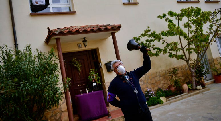 Begona Diaz, 58, looks at her husband, Jose Mari Perez, 59, a member of "Santa Vera Cruz'' brotherhood known as ''Los Picaos'' wearing a mask for protection while ringing a bell outside of his house on Maundy Thursday after celebrations were cancelled due