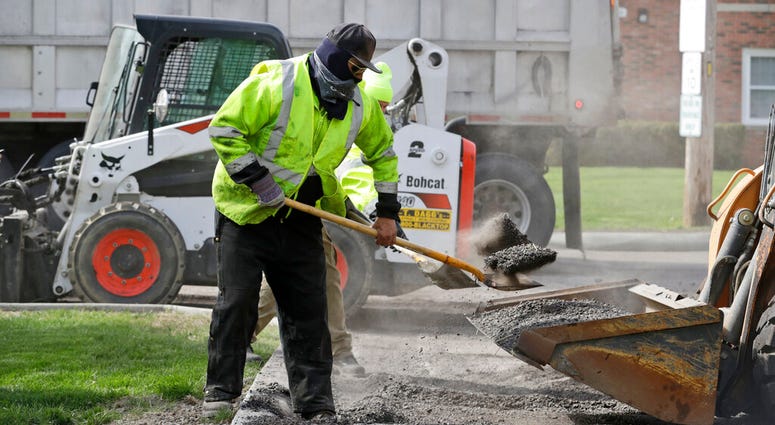 FILE - In this May 6, 2020 file photo, Jarrett Barth, who works for Dagg's Asphalt & Sealcoating, shovels gravel into a backhoe bucket in Lyndhurst, Ohio.