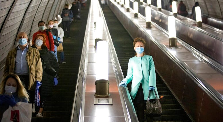 People wearing face masks and gloves to protect against coronavirus, observe social distancing guidelines as they go down the subway on the escalator in Moscow, Russia, Tuesday, May 12, 2020.