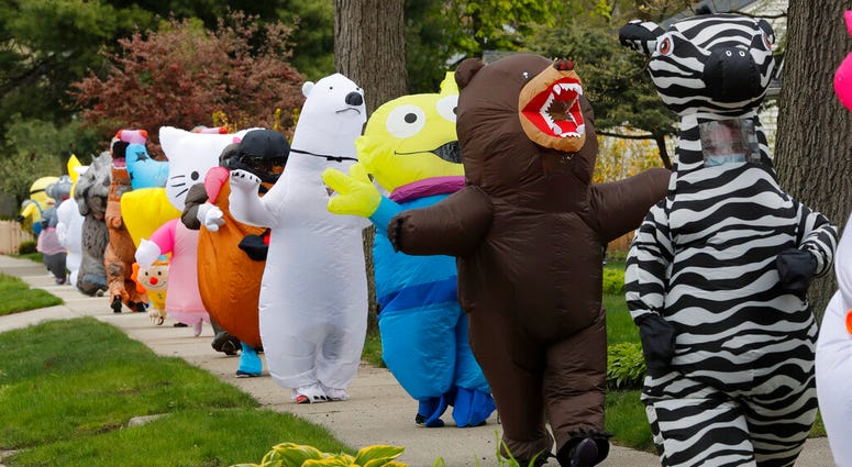 In this Monday, May 11, 2020 photo, members of the T-Rex Walking Club walk through a neighborhood in Ferndale, Mich. While the club members get a kick out of their strolls through town, the idea is to bring a little bit of cheer to their fellow residents