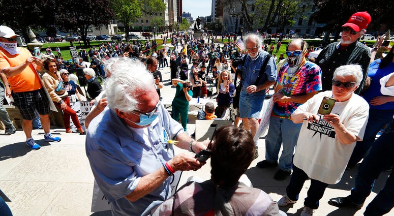 Barber Karl Manke, of Owosso, gives a free haircut on the steps of the State Capitol during a rally in Lansing, Mich., Wednesday, May 20, 2020.