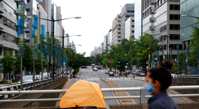 A homeless person's tent sits above a quiet K Street Northwest as a woman wearing a face mask to protect against the spread of the new coronavirus walks past, Thursday, May 21, 2020, in Washington.