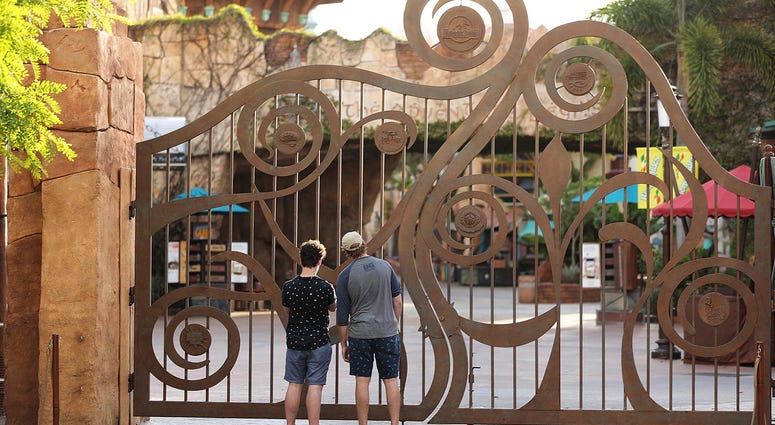 FILE - In this Thursday, May 14, 2020, file photo, guests peer through the closed gate to Universal's Islands of Adventure beside Universal CityWalk, in Orlando, Fla.