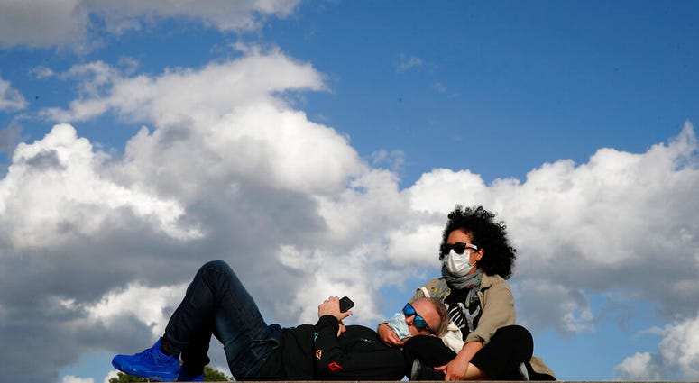 Parisians, wearing protective masks, sit in the sun along the closed Tuileries garden in Paris, Saturday, May 23, 2020 as France gradually lifts its COVID-19 lockdown.