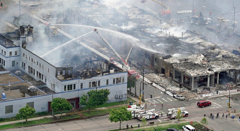 Firefighters work on an apartment building under construction, Thursday, May 28, 2020, tentatively known as Midtown Corner, left, after it was burned to the ground in Minneapolis, Minn.