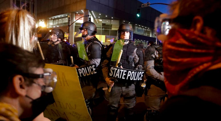 Protesters stand in front of Kentucky State Police officers as they protest the deaths of George Floyd and Breonna Taylor, Friday, May 29, 2020, in Louisville, Ky. Breonna Taylor, a black woman, was fatally shot by police in her home in March.