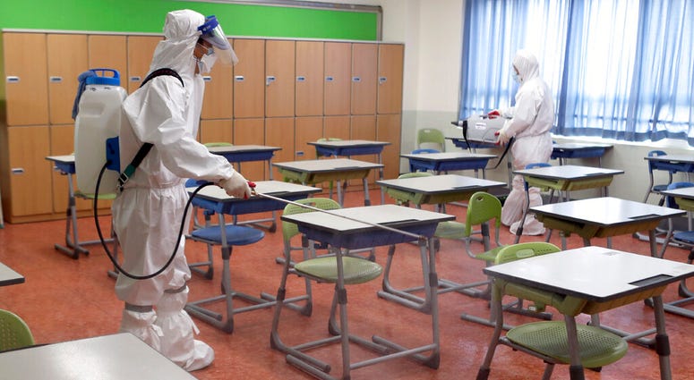 Workers wearing protective gear disinfect as a precaution against the new coronavirus in a class at a high school in Busan, South Korea, Saturday, May 30, 2020.