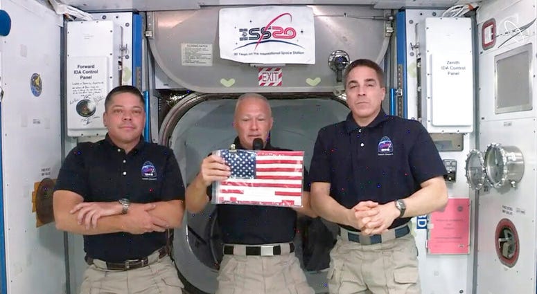 In this image taken from NASA video on Monday, June 1, 2020, NASA astronauts Robert L. Behnken, left, and Chris Cassidy right, listen as commander Douglas Hurley speaks about retrieving the American flag left behind at the International Space Station near