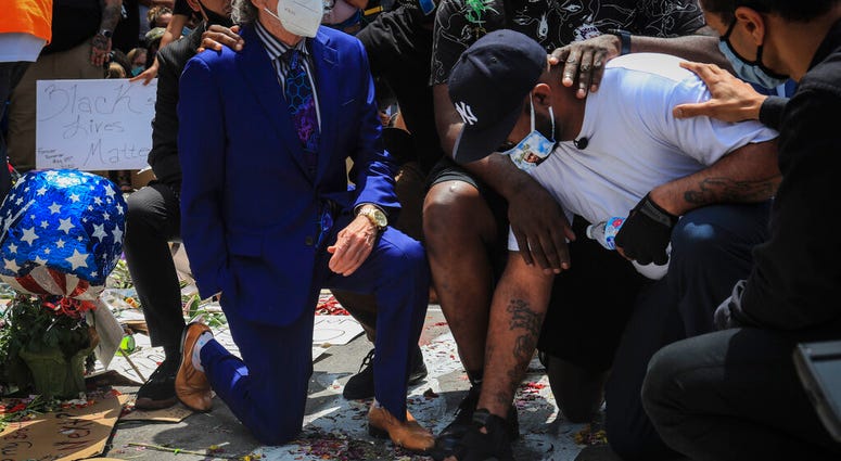 An emotional Terrence Floyd, second from right, is comforted as he touch the spot at the intersection of 38th Street and Chicago Avenue, Minneapolis, Minn., where his brother George Floyd, encountered police and died while in their custody, Monday, June 1