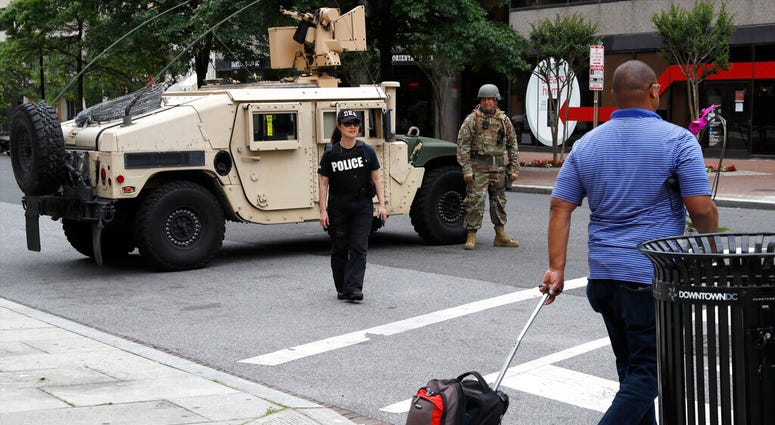 A man walks through an intersection blocked by a military humvee from DC National Guard and a DEA police officer as demonstrators gather to protest the death of George Floyd, Tuesday, June 2, 2020, in Washington.