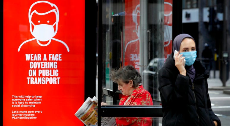 Passengers wait at a bus stop with a sign advising travellers to wear a face covering whilst travelling, in London, Friday, June 5, 2020.