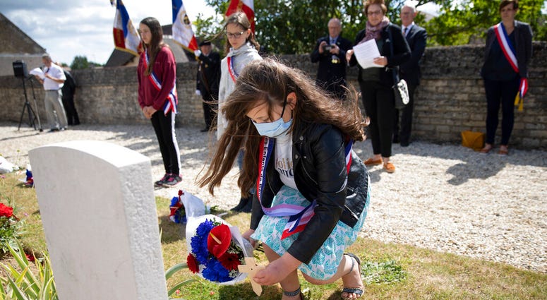 British expatriate Steven Oldrid, left, directs people where to lay wooden crosses with names of WWII dead and flowers during D-Day ceremonies at the local war cemetery in Benouville, Normandy, France on Saturday, June 6, 2020.