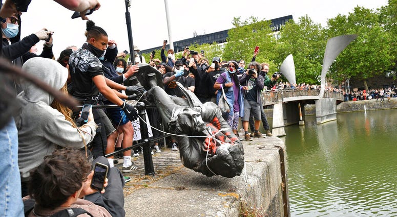 Protesters throw a statue of slave trader Edward Colston into Bristol harbour, during a Black Lives Matter protest rally, in Bristol, England, Sunday June 7, 2020, in response to the recent killing of George Floyd by police officers in Minneapolis, USA, t